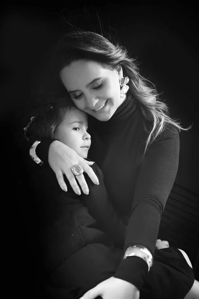 Mãe abraçando a filha com carinho, em retrato preto e branco sobre fundo escuro