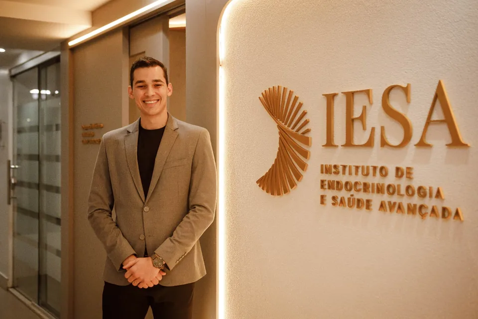 Profissional de blazer em pé ao lado da recepção com logotipo iluminado