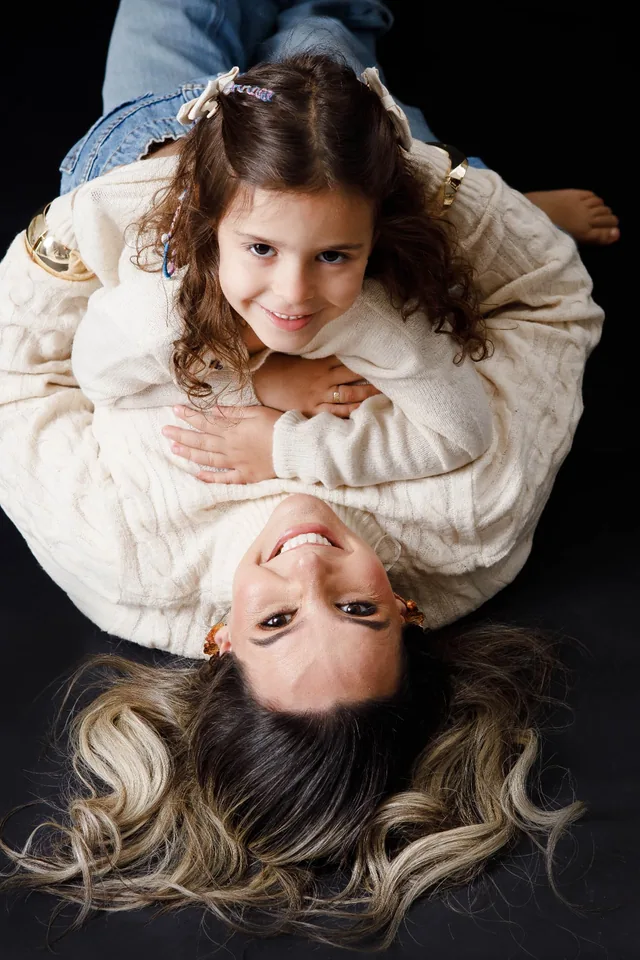 Mãe e filha deitadas no chão, de cabeças invertidas, sorrindo para a câmera