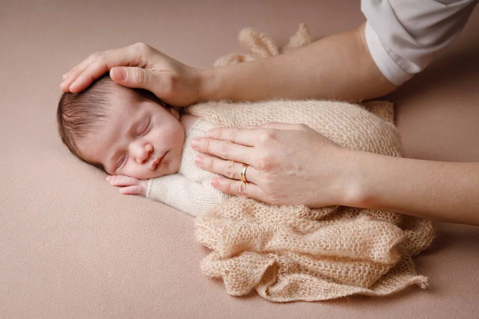 Mãos dos pais acariciando o recém-nascido que dorme envolto em manta de tricô bege