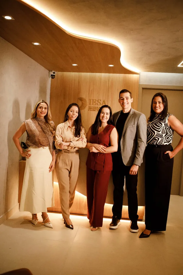Equipe de cinco profissionais em pé na recepção, sob iluminação quente