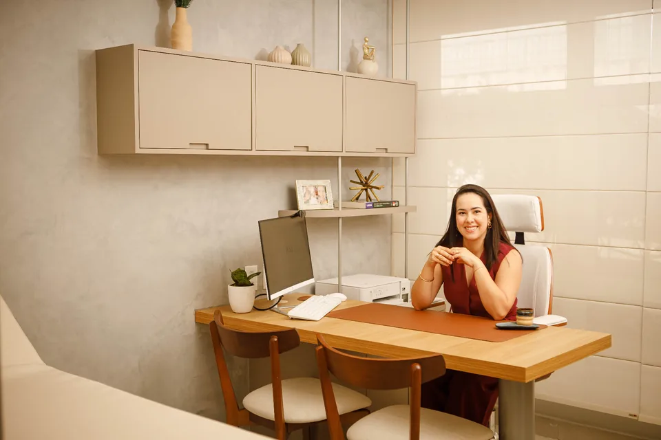 Profissional sentada à mesa em consultório claro e organizado, sorrindo