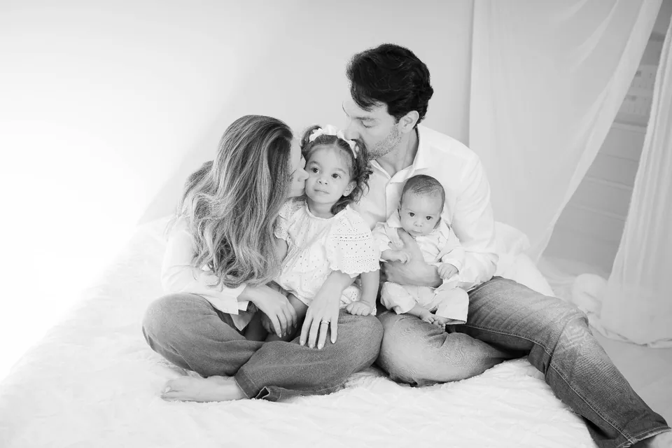 Família reunida sentada na cama, em fotografia preto e branco